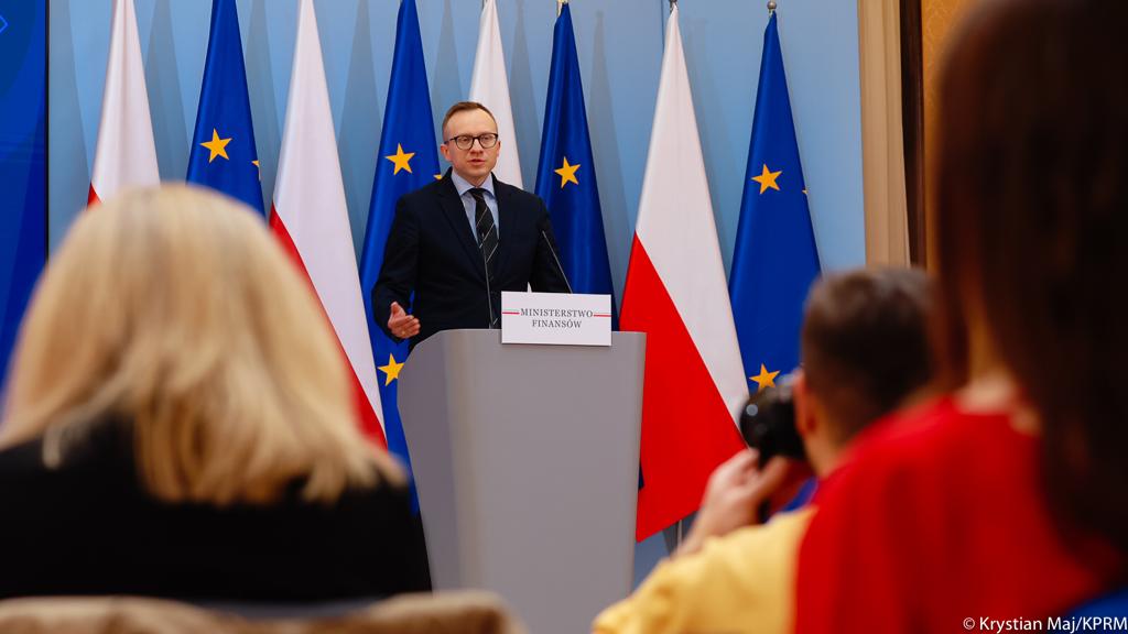 Wiceminister finansów Artur Soboń podczas wystąpienia, w tle flagi Polski i Unii Europejskiej.