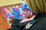Funkcjonariuszka Służby Celno-Skarbowej w gumowych rękawiczkach wyjmuje z opakowania zbiorczego zabawki w jaskrawych kolorach i z bliska je ogląda.